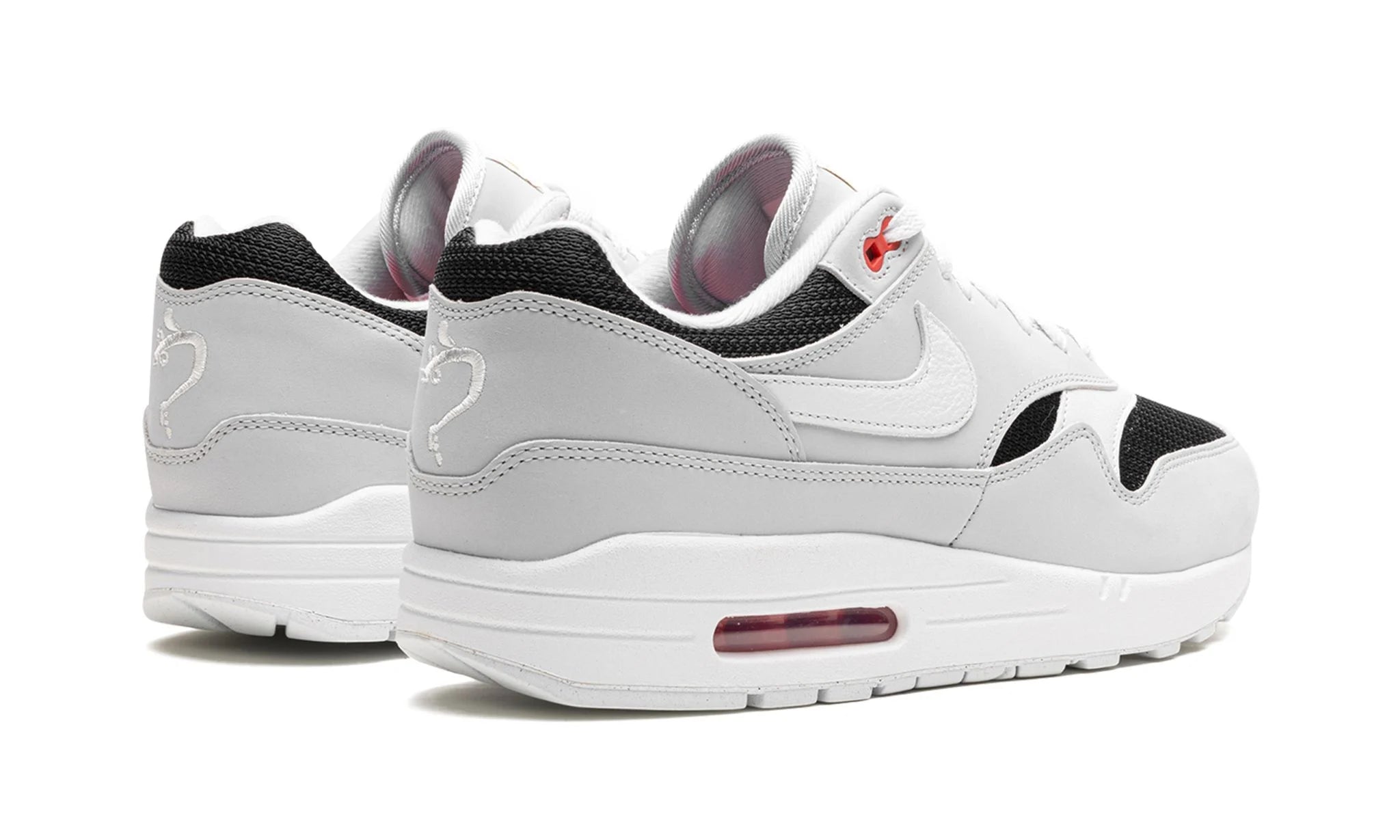 Nike Air Max 1 “Urawa 2023” (FD9081-001) sneakers met een grijze basis, bordeauxrode accenten en zwarte details, premium mesh en suède overlays, en de iconische zichtbare Air unit in de zool.