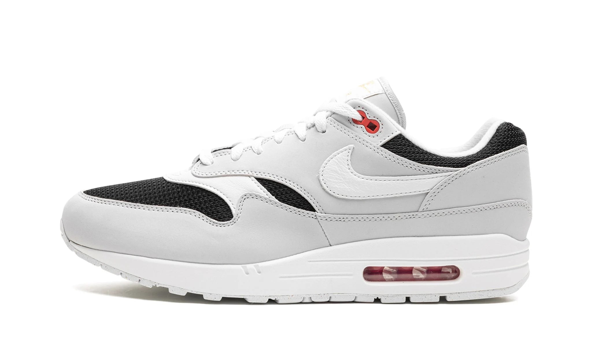 Nike Air Max 1 “Urawa 2023” (FD9081-001) sneakers met een grijze basis, bordeauxrode accenten en zwarte details, premium mesh en suède overlays, en de iconische zichtbare Air unit in de zool.