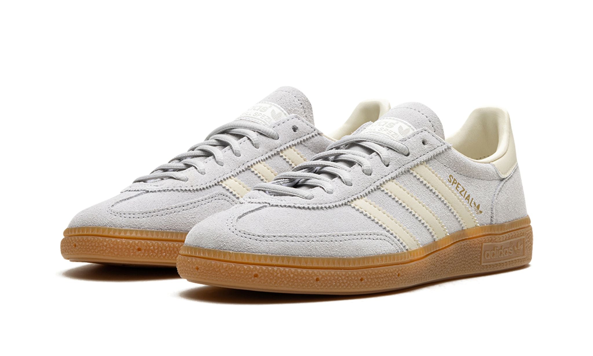 adidas Handball Spezial (IF7086) sneakers in een grijs en crème wit kleurenschema, uitgevoerd in zacht suède met de kenmerkende witte drie strepen, gum rubber zool en een klassiek low top retro silhouet.
